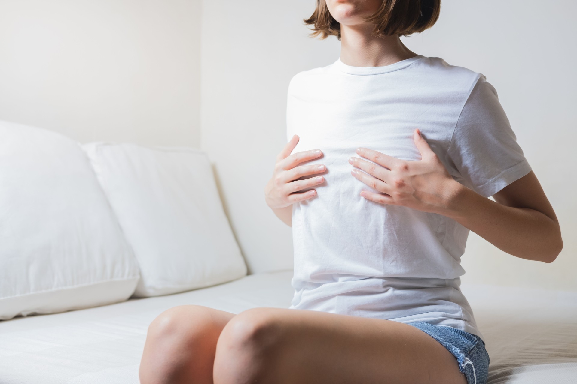 Woman sits on a bed and holds her breasts